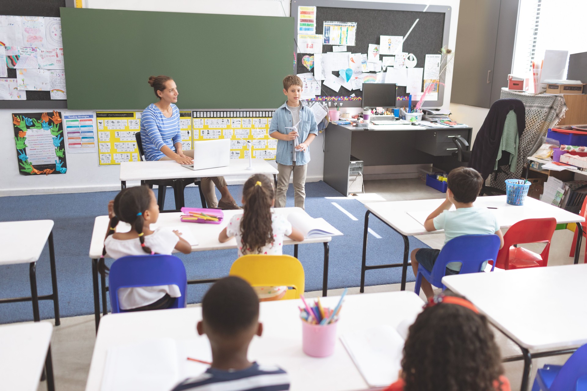 Schoolboy explaining about windmill in front of his classmates while her teacher listening him
