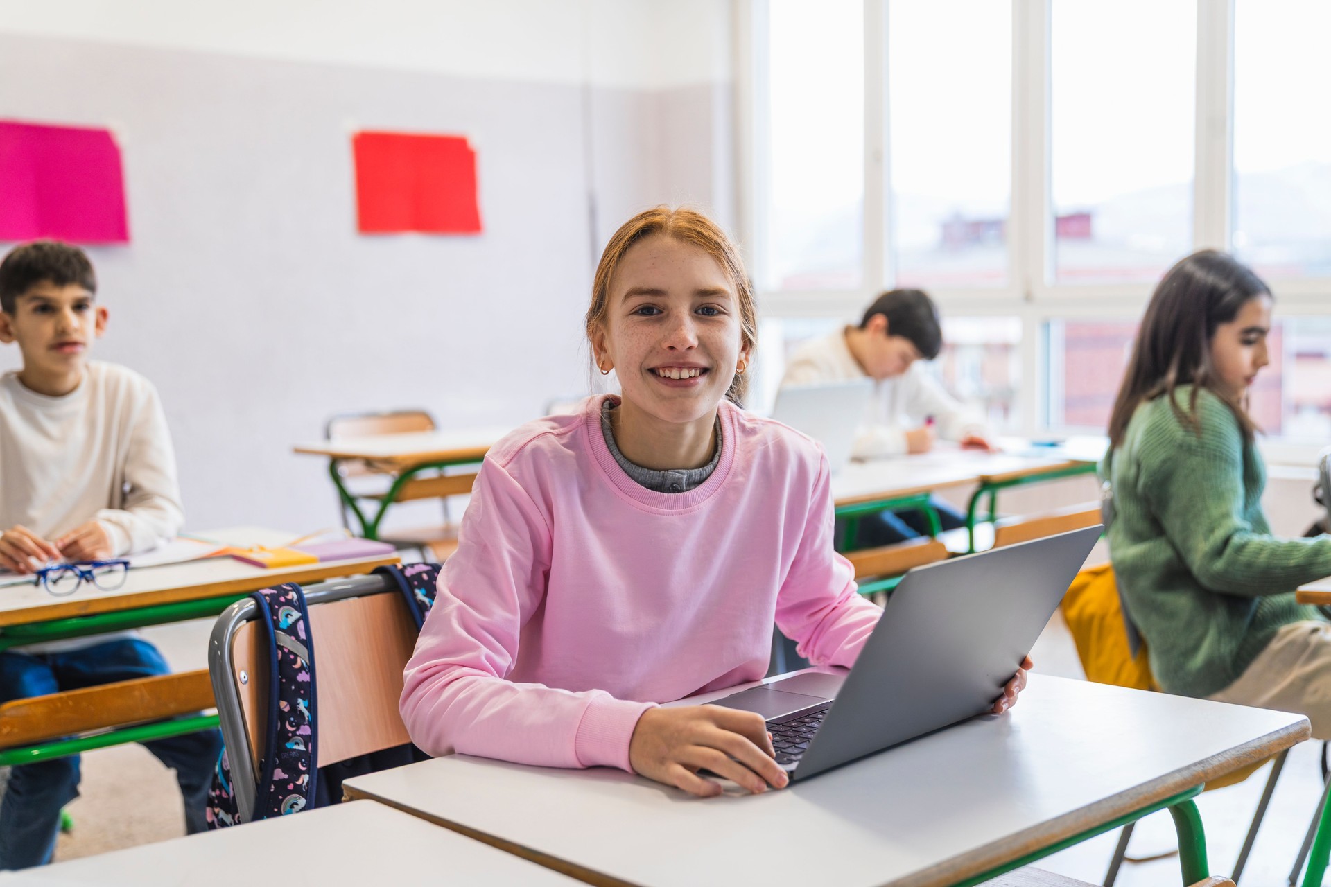 Smiling student using laptop in classroom with classmates